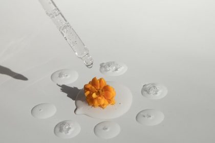 pipette with transparent essence and yellow flower on white surface