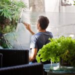 man in gray shirt cleaning clear glass wall near sofa